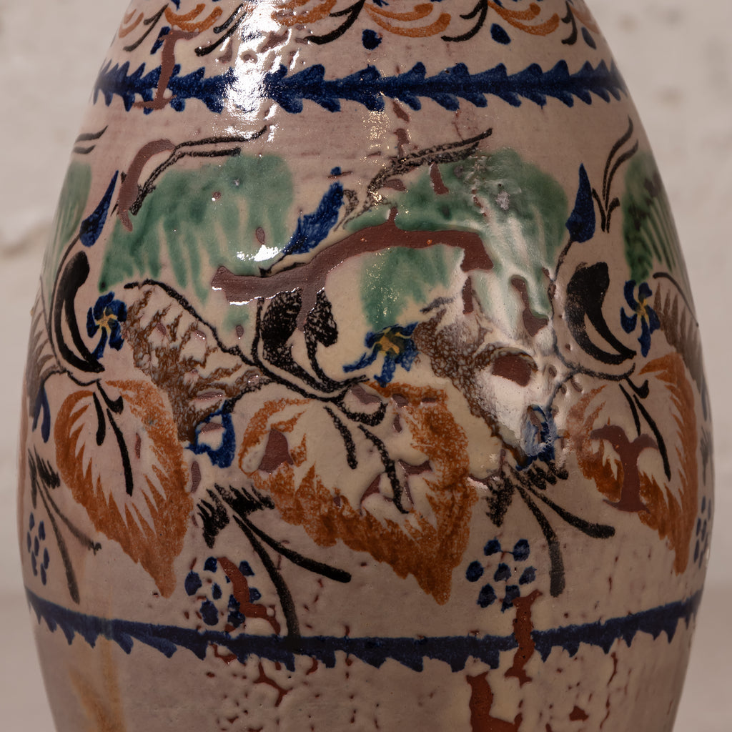 Close-up of a ceramic vase or bottle with a glossy beige glaze and hand-painted floral and bird motifs in blue, green, brown, and black.
