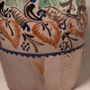 Close-up of a ceramic vase or pot with a hand-painted floral pattern in blue, brown, and green on a warm off-white glaze.