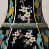 Close-up of a glossy black ceramic vase decorated with white plum blossoms, yellow flowers, and turquoise blue leaves, featuring a patterned turquoise and gold band around the neck.