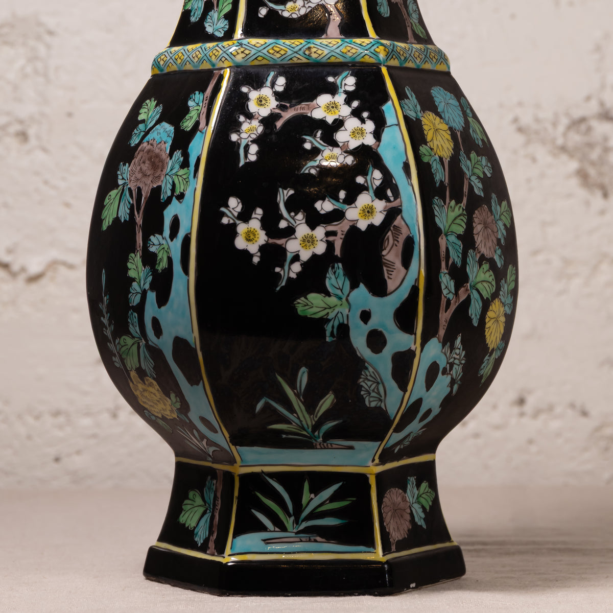 A decorative ceramic vase with a glossy black glaze, featuring hand-painted floral motifs in white, yellow, green, and brown, accented with turquoise blue and gold details.