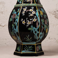 A decorative ceramic vase with a glossy black glaze, featuring hand-painted floral motifs in white, yellow, green, and brown, accented with turquoise blue and gold details.