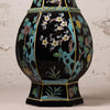 A decorative ceramic vase with a glossy black glaze, featuring hand-painted floral motifs in white, yellow, green, and brown, accented with turquoise blue and gold details.