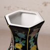 Close-up of a hexagonal ceramic vase with a glossy black exterior decorated with colorful floral patterns in blue, yellow, and brown, featuring a white glazed interior.