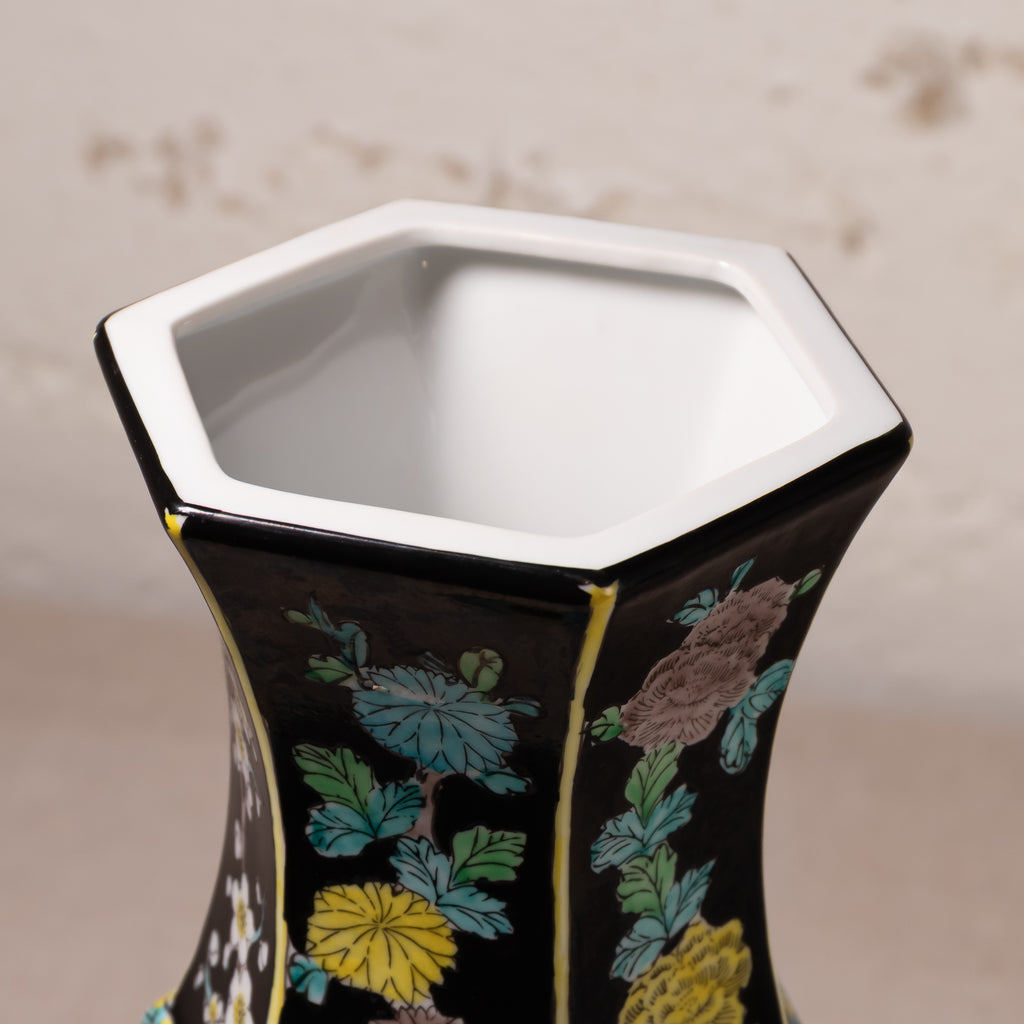 Close-up of a hexagonal ceramic vase with a glossy black exterior decorated with colorful floral patterns in blue, yellow, and brown, featuring a white glazed interior.