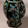 A close-up of a decorative ceramic vase with a glossy black glaze, featuring hand-painted floral motifs in turquoise, green, white, yellow, and pink, outlined with gold trim.