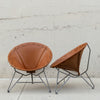 Two mid-century modern butterfly chairs with brown leather seats and silver metal legs, displayed against a light concrete wall.