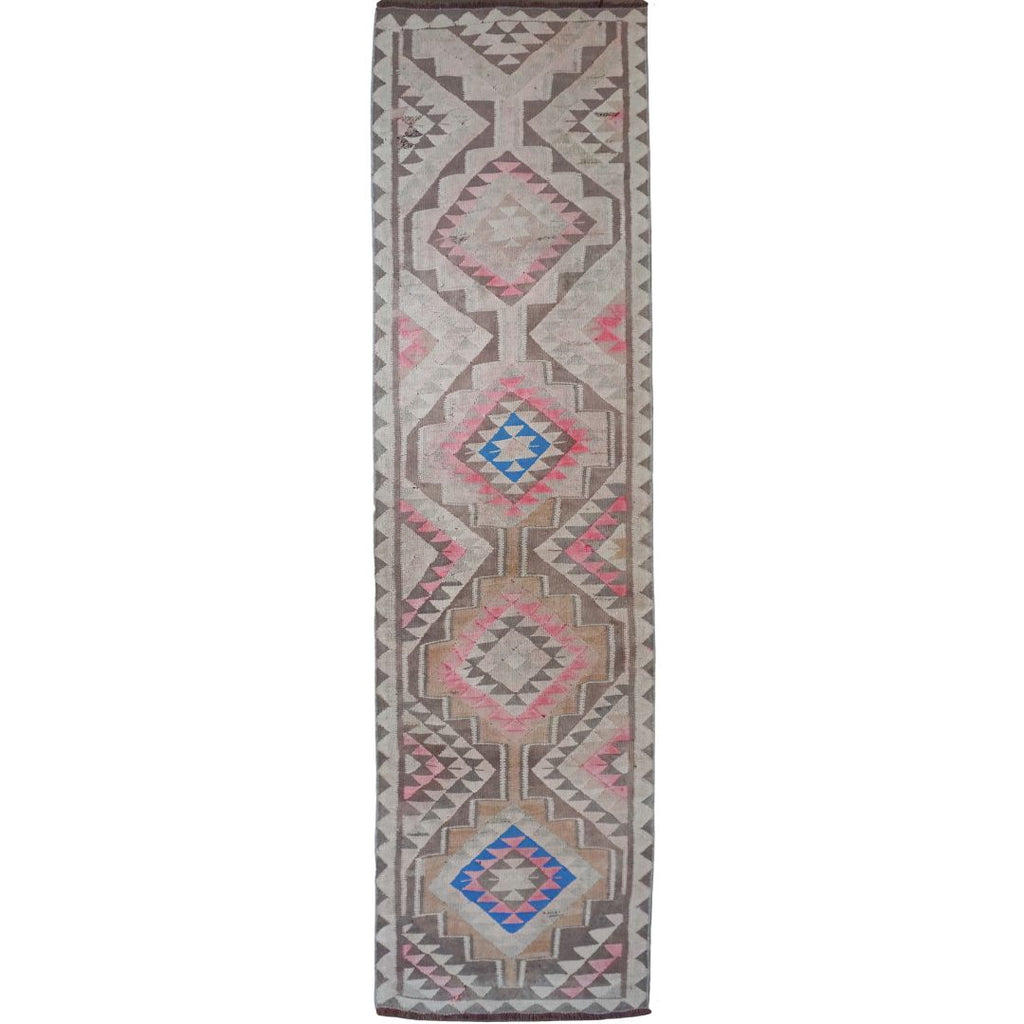 A long rectangular area rug with a geometric tribal pattern in pink, blue, gray, and beige on a white background.