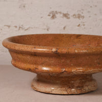 A terracotta-colored stone planter with a textured, speckled finish and a flared rim, shown on a neutral surface against a rustic, light-colored wall.