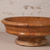 A terracotta-colored stone planter with a textured, speckled finish and a flared rim, shown on a neutral surface against a rustic, light-colored wall.