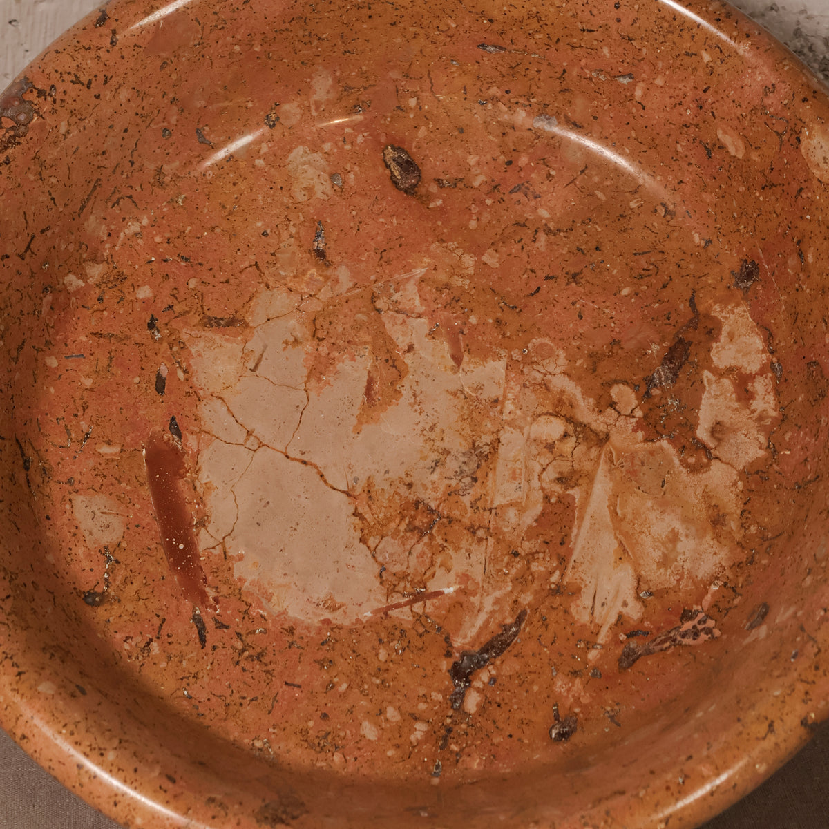A close-up of a terracotta-colored ceramic bowl or dish with a textured, speckled finish and a lighter beige chipped area near the center.