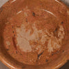 A close-up of a terracotta-colored ceramic bowl or dish with a textured, speckled finish and a lighter beige chipped area near the center.