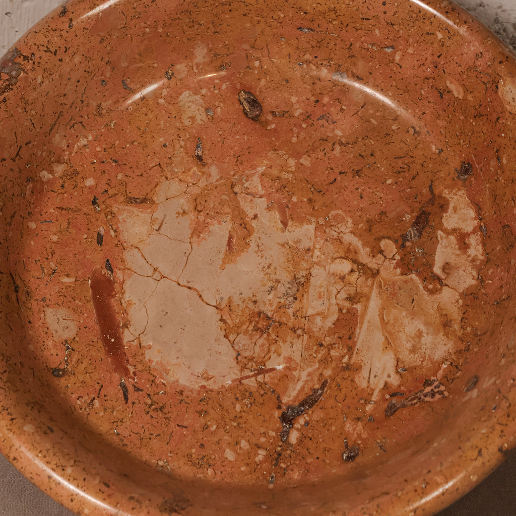 A close-up of a terracotta-colored ceramic bowl or dish with a textured, speckled finish and a lighter beige chipped area near the center.