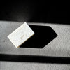 A rectangular white bar of soap with embossed text and a small row of dots, photographed on a textured gray surface with dramatic diagonal shadows against a black background.