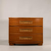 A mid-century modern three-drawer chest of drawers made of warm medium-brown wood with decorative inset drawer pulls, photographed against a neutral light gray background.