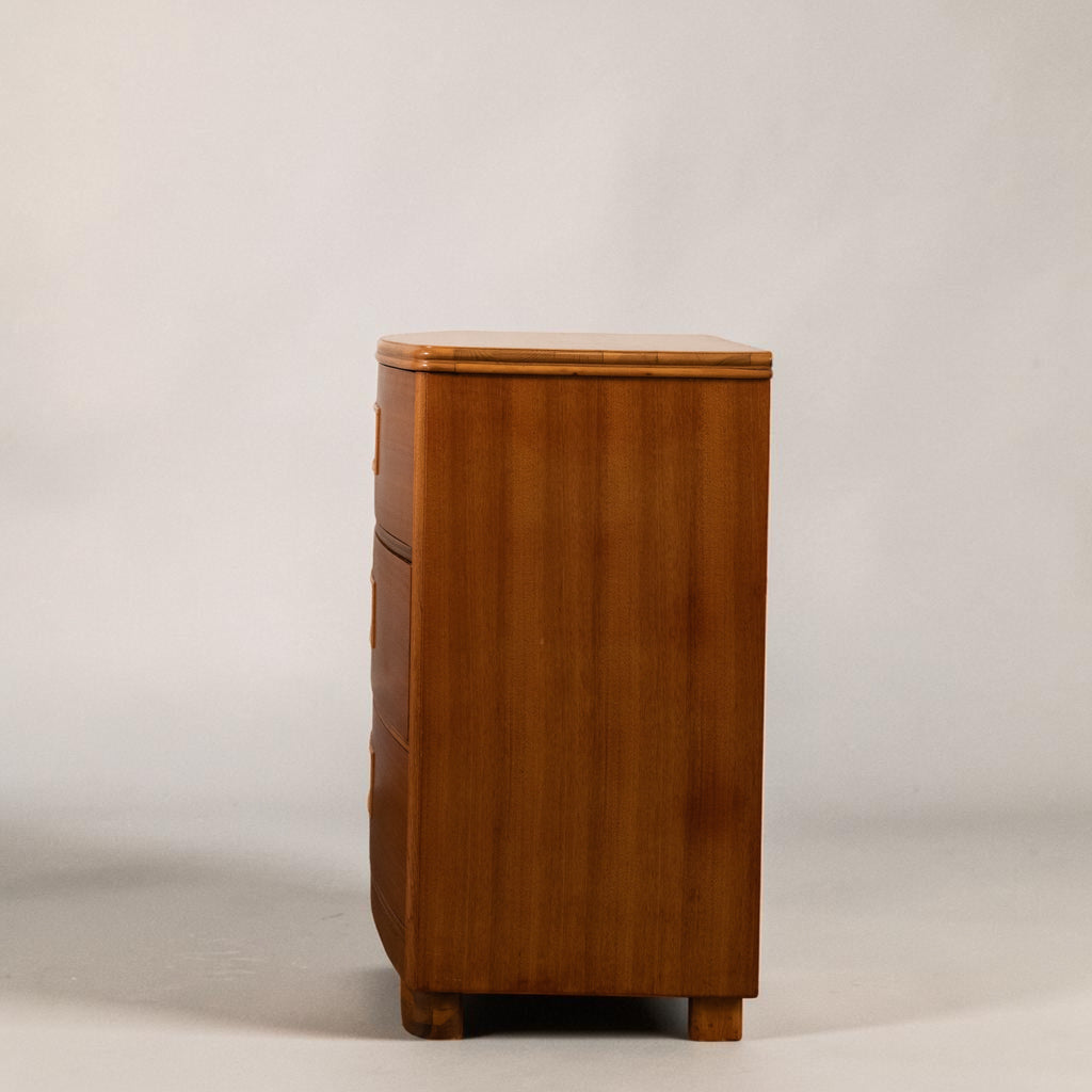A mid-century modern wooden chest of drawers with a warm honey-brown finish, shown from a side profile view against a neutral light gray background.