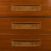 Close-up of a wooden chest of drawers showing three drawers with rectangular glass-front fronts and decorative inlay.