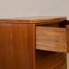 Close-up of a warm medium-brown wooden cabinet with a curved top and an open drawer showing dovetail joint construction.