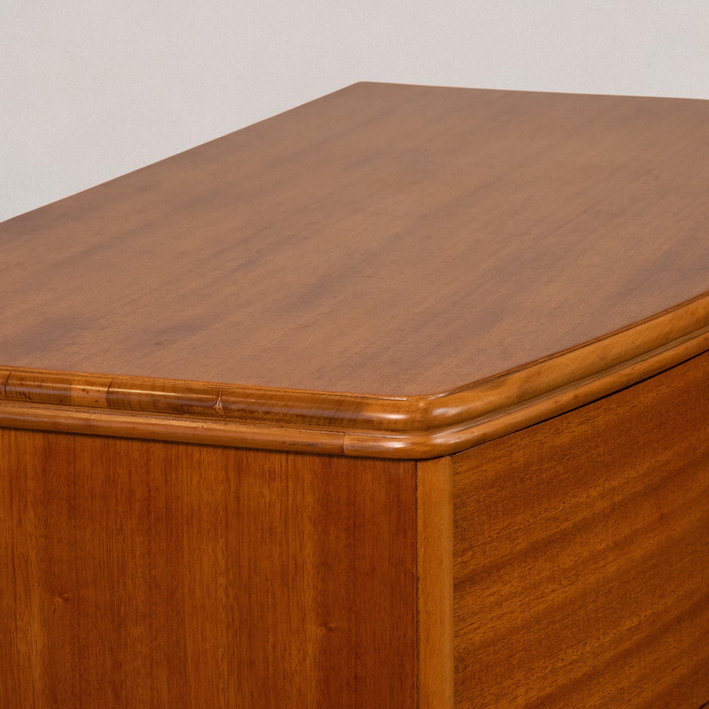 Close-up of a wooden cabinet or dresser showing the top surface, rounded corner trim, and wood grain finish against a plain light background.