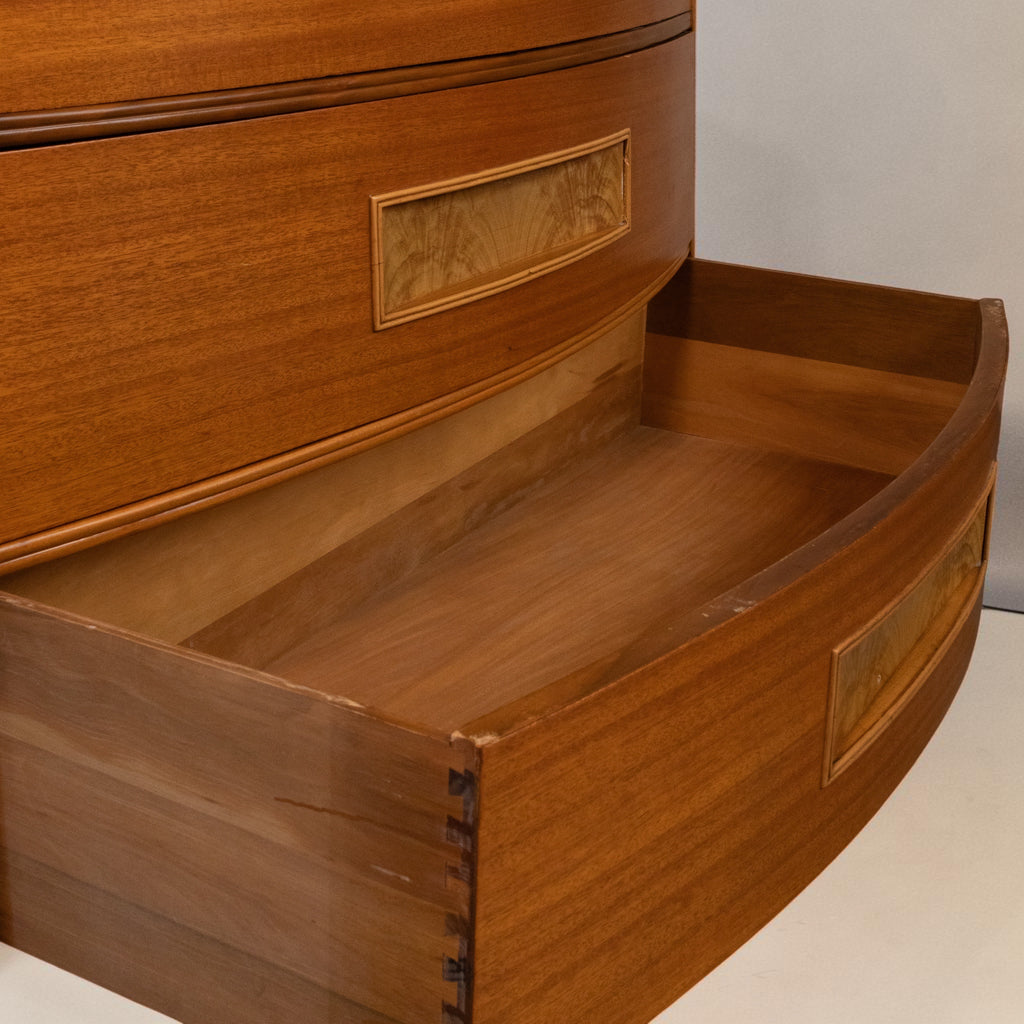 Close-up of a curved wooden drawer front with a partially pulled-out drawer, showing warm medium-brown wood grain and a decorative inset panel.