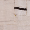 A close-up of a textured woven rug or textile in warm off-white/cream with a dark brown horizontal stripe and a small yellow-green accent near the center.
