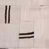 A close-up of a patchwork textile made from off-white woven fabric squares with dark brown striped accents.
