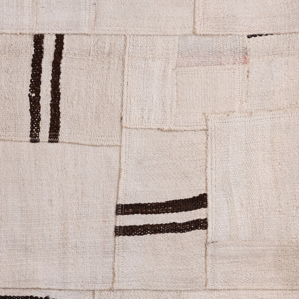 A close-up of a patchwork textile made from off-white woven fabric squares with dark brown striped accents.