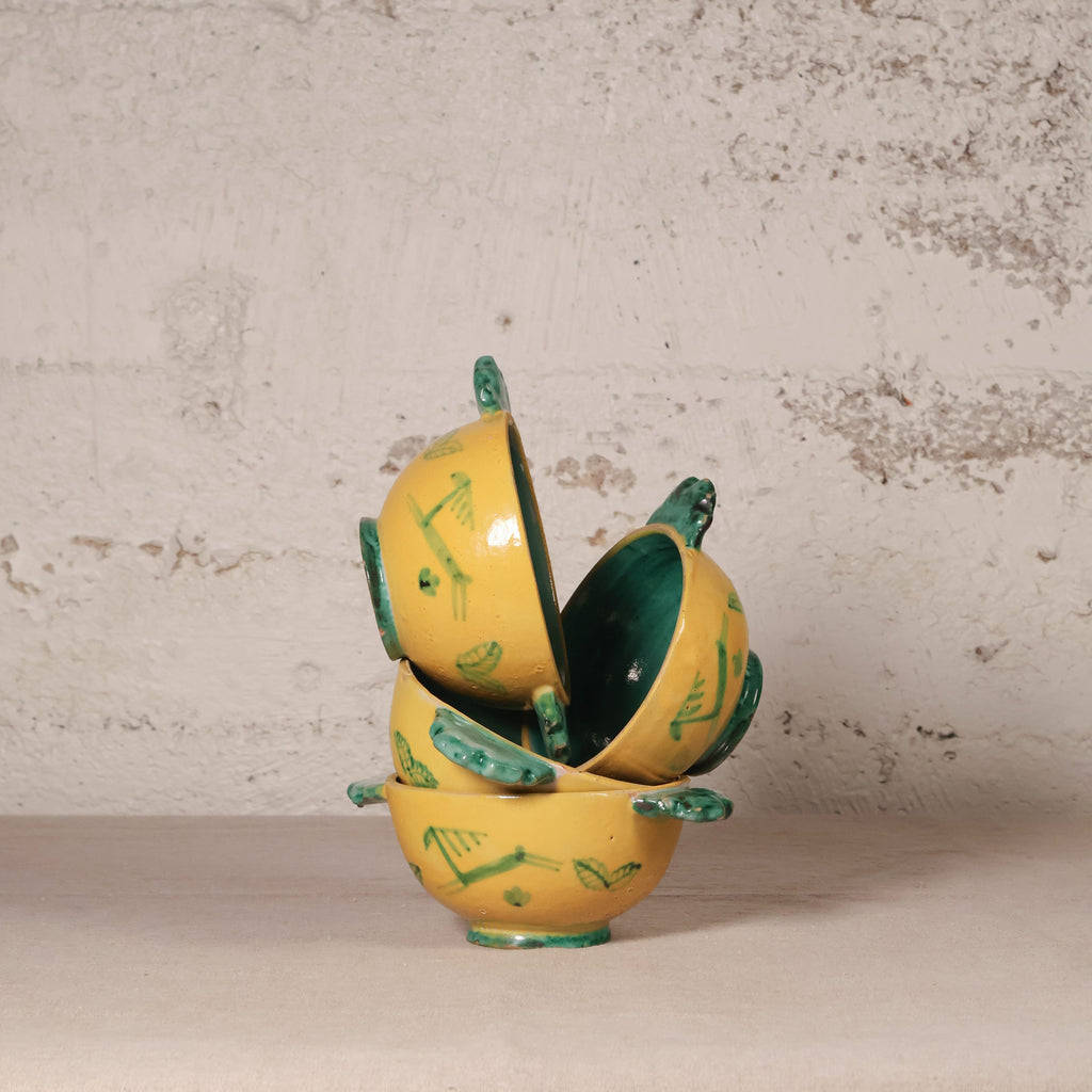Yellow ceramic bowl with green accents on a textured surface
