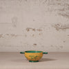 Yellow ceramic bowl with green interior and handles on a textured surface with a beige background