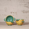 Two ceramic bowls with green interior and yellow exterior on a textured surface.