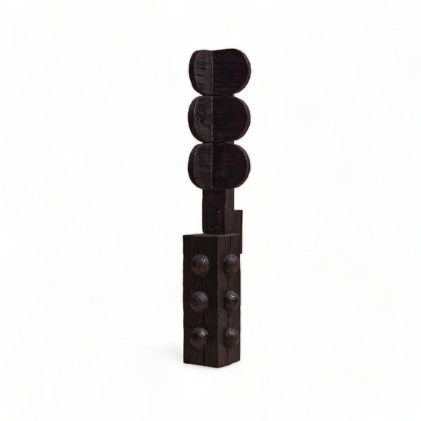 A dark brown wooden sculpture of a traffic light with three circular signal lights on top and a rectangular base with raised circular details, set against a plain white background.