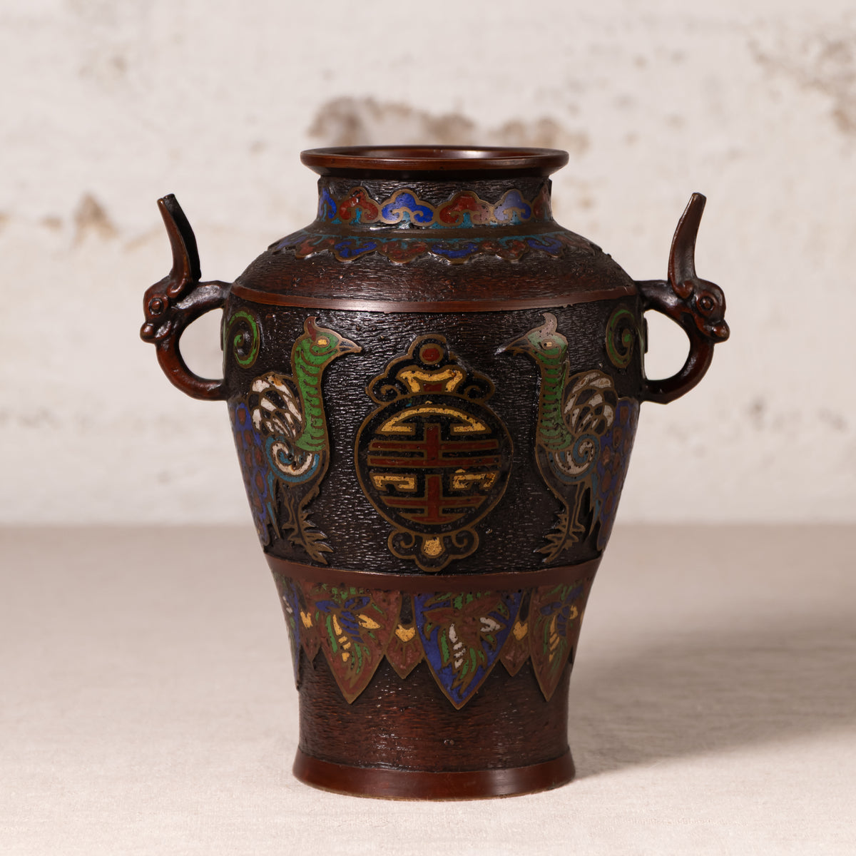 An antique Japanese enamel vase with dragon handles, featuring a dark bronze-brown base with vibrant green, blue, and gold decorative details.