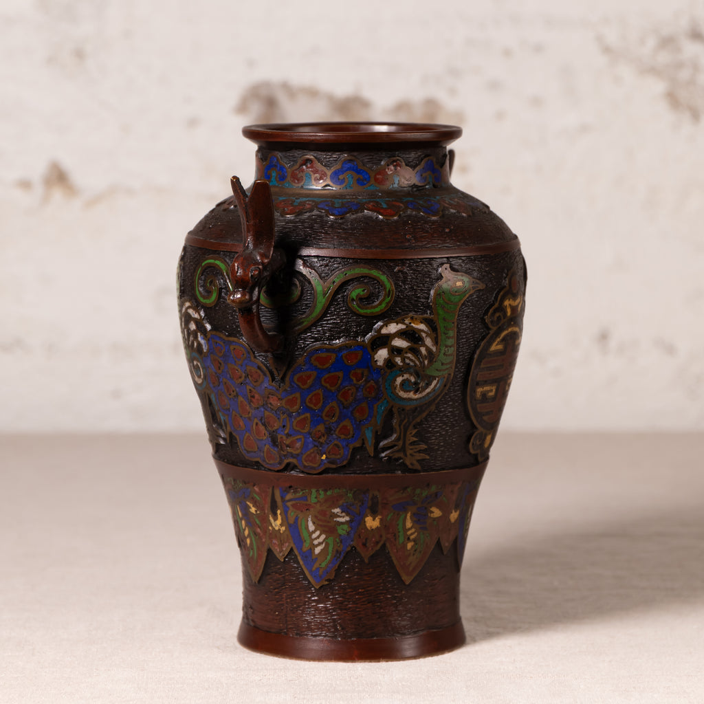 An antique Japanese cloisonne enamel vase with a dark brown lacquered base, featuring vibrant blue, green, and gold floral and dragon motifs, set against a neutral textured beige background.