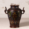 An antique-style Japanese cloisonné bronze vase with dragon handles and phoenix motifs, displayed on a light beige surface against a textured off-white background.