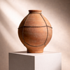 A terracotta clay vase with decorative dark cord wrapped lines, displayed on a white pedestal against a warm beige background with soft diagonal shadows.