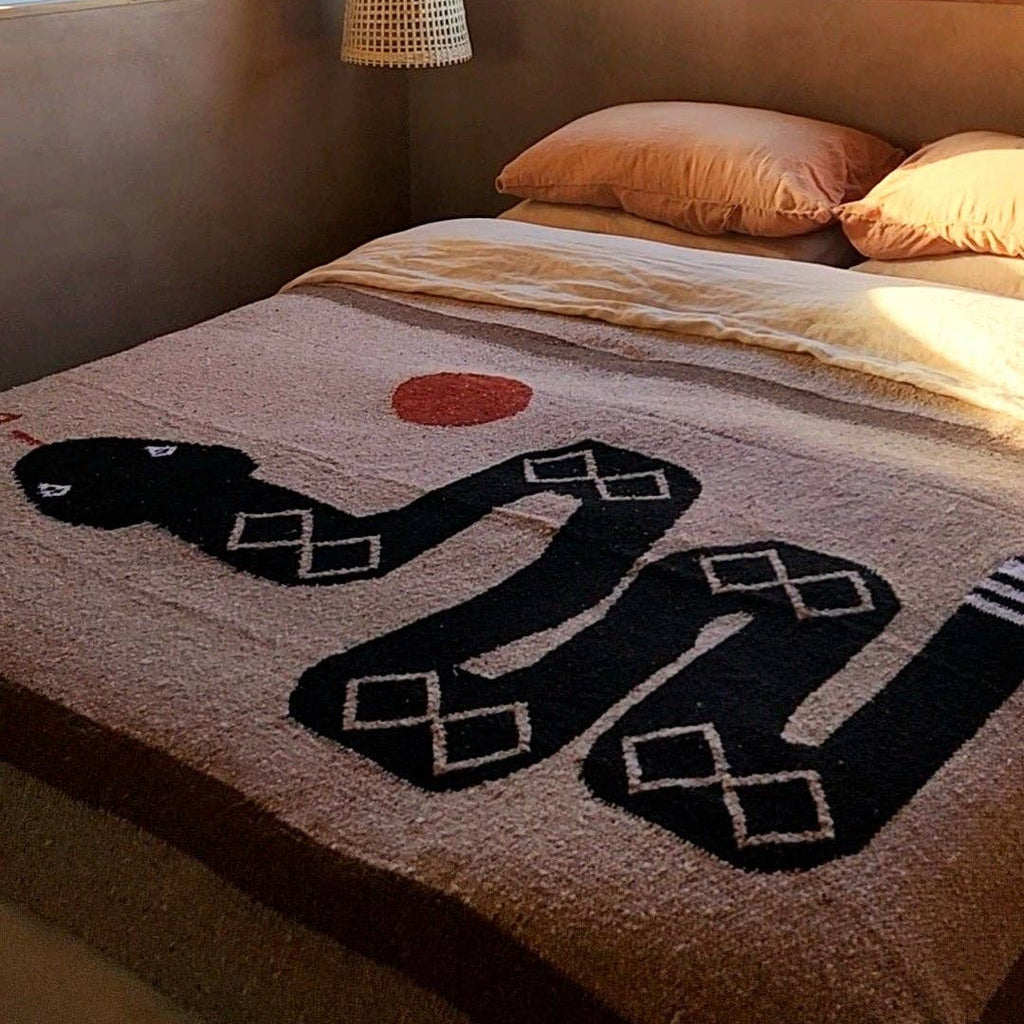 Bed with a decorative blanket featuring a snake design in a room with large windows.