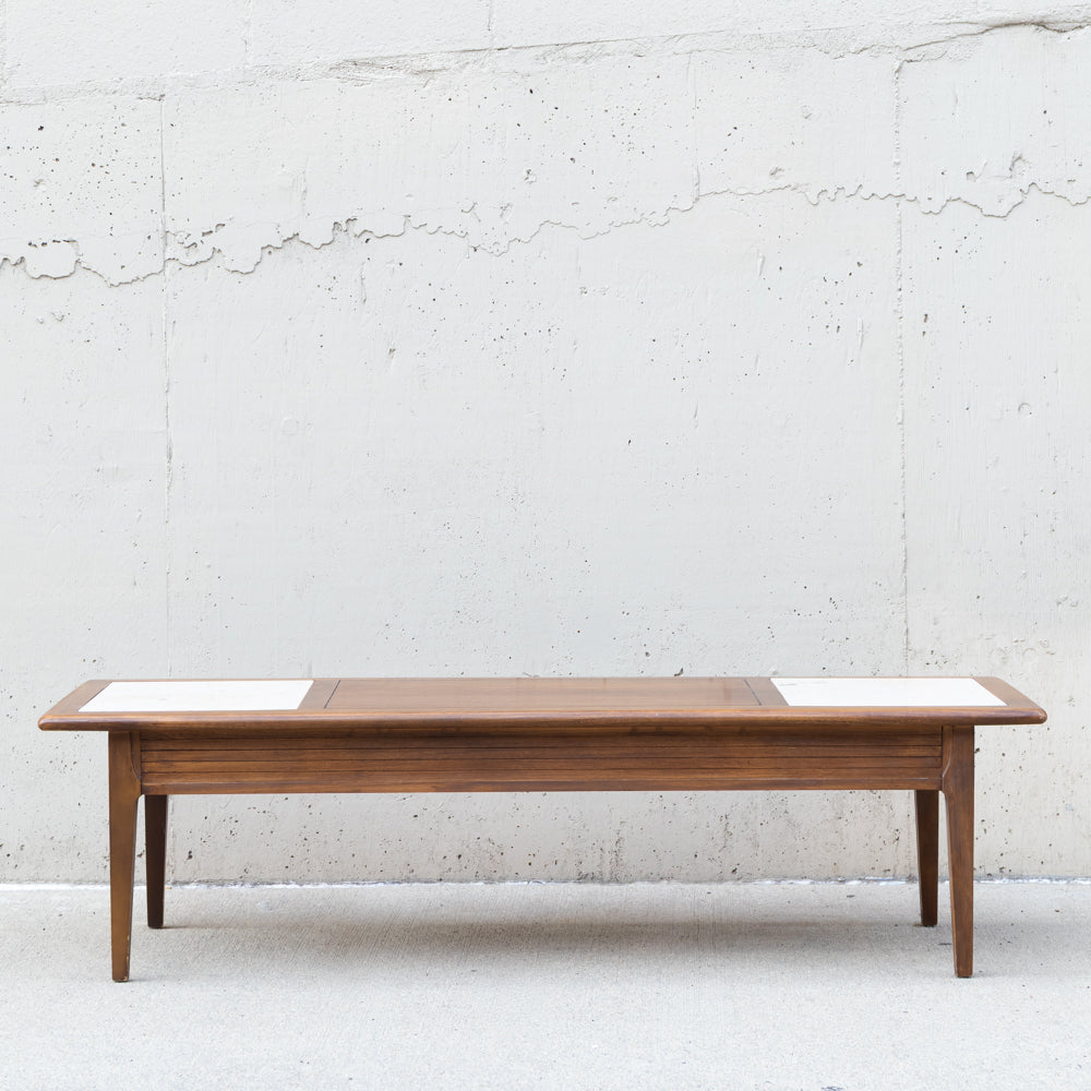 A mid-century modern wooden coffee table with a warm brown wood grain finish and two white rectangular inlay panels on the top, set against a textured white concrete wall.