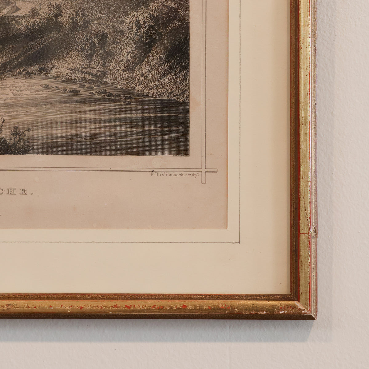Framed vintage landscape print with a gold border on a textured wall.