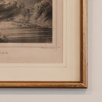 Framed vintage landscape print with a gold border on a textured wall.