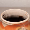 Close-up of the interior rim of a ceramic jar or vase, showing a warm off-white glazed interior with dark brown interior staining and a terracotta orange exterior visible at the bottom.