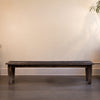 Wooden bench against a plain wall with a plant in the corner