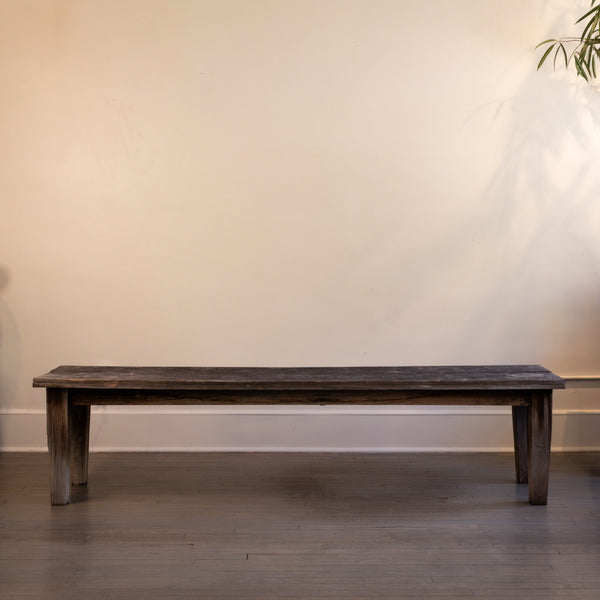 Wooden bench against a plain wall with a plant in the corner