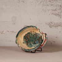 Ceramic plate with fish design on a stand against a textured wall.