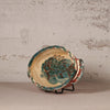 Ceramic plate with fish design on a stand against a textured wall.