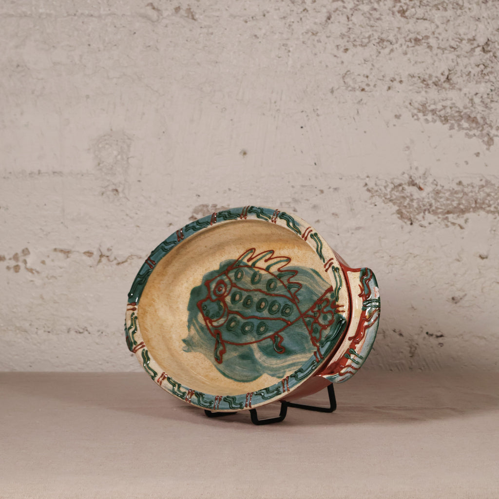 Ceramic plate with fish design on a stand against a textured wall.