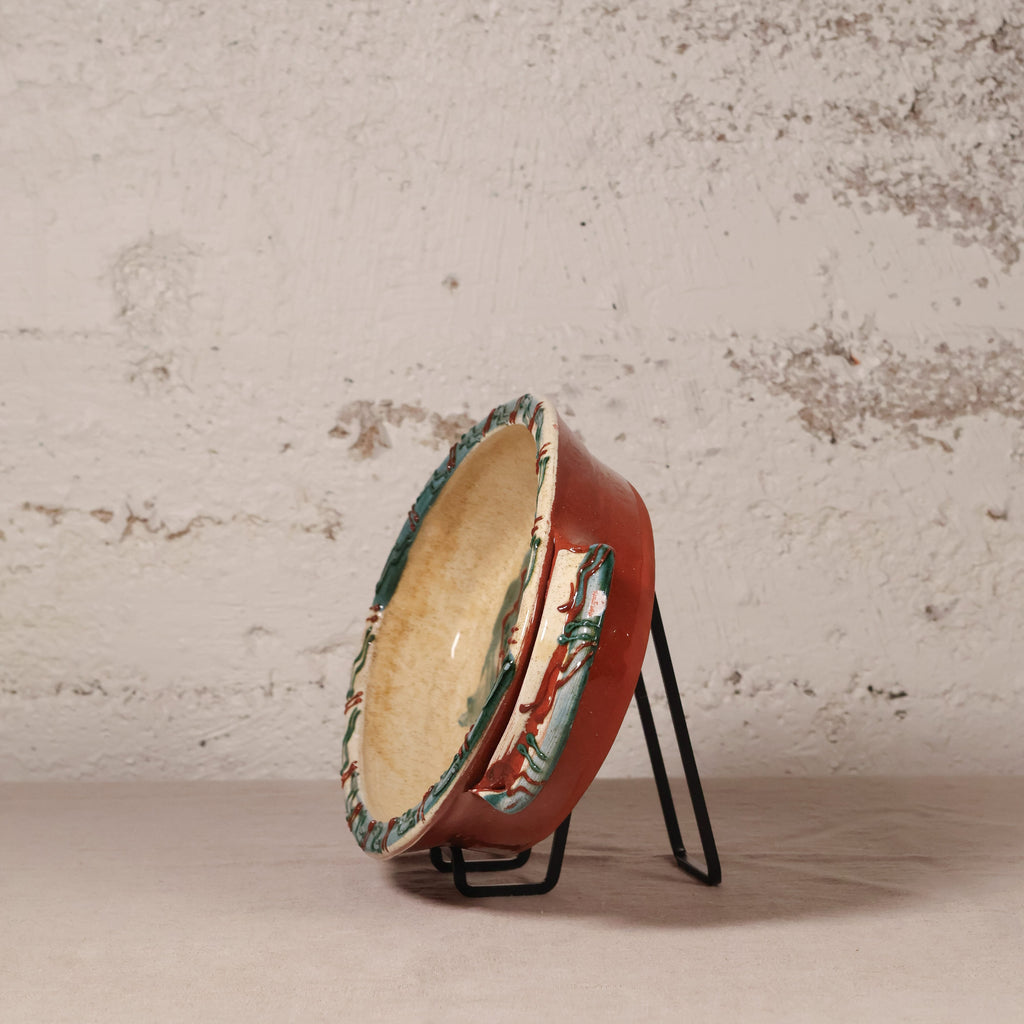 Decorative ceramic bowl with a floral pattern on a stand against a textured wall.