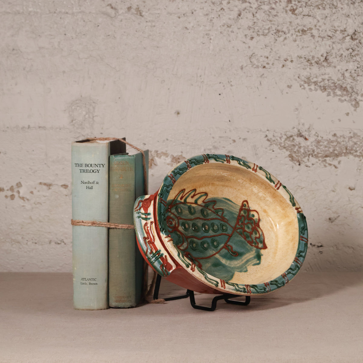 Ceramic plate with fish design next to two books on a textured surface.