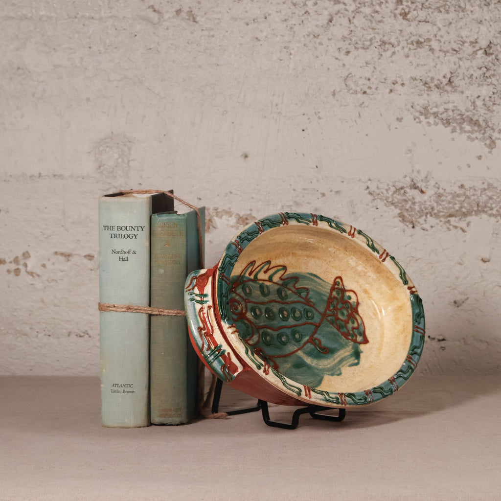 Ceramic plate with fish design next to two books on a textured surface.