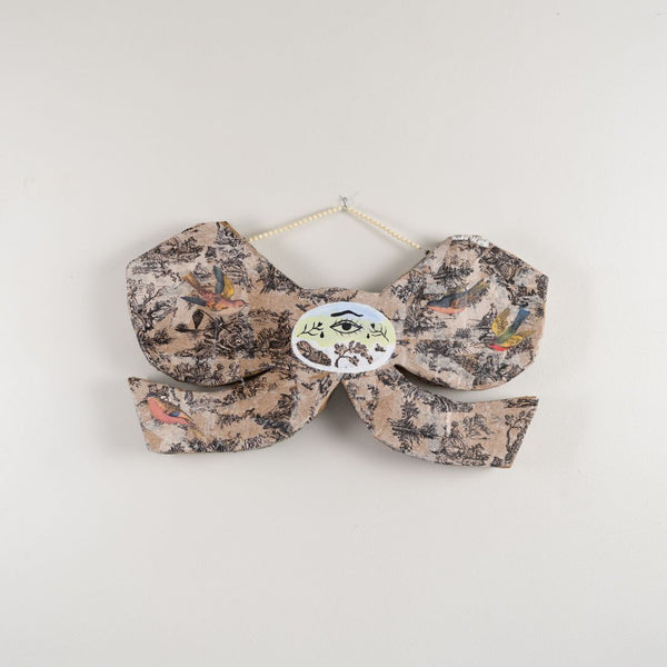 Floral-patterned bow tie with a brand label on a light gray background