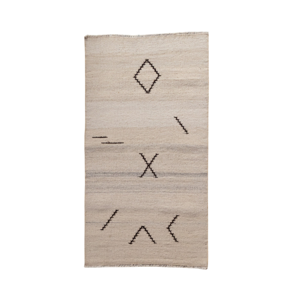 A rectangular beige woven rug with a minimalist black geometric pattern, including a diamond, an X, and diagonal lines, shown against a plain white background.