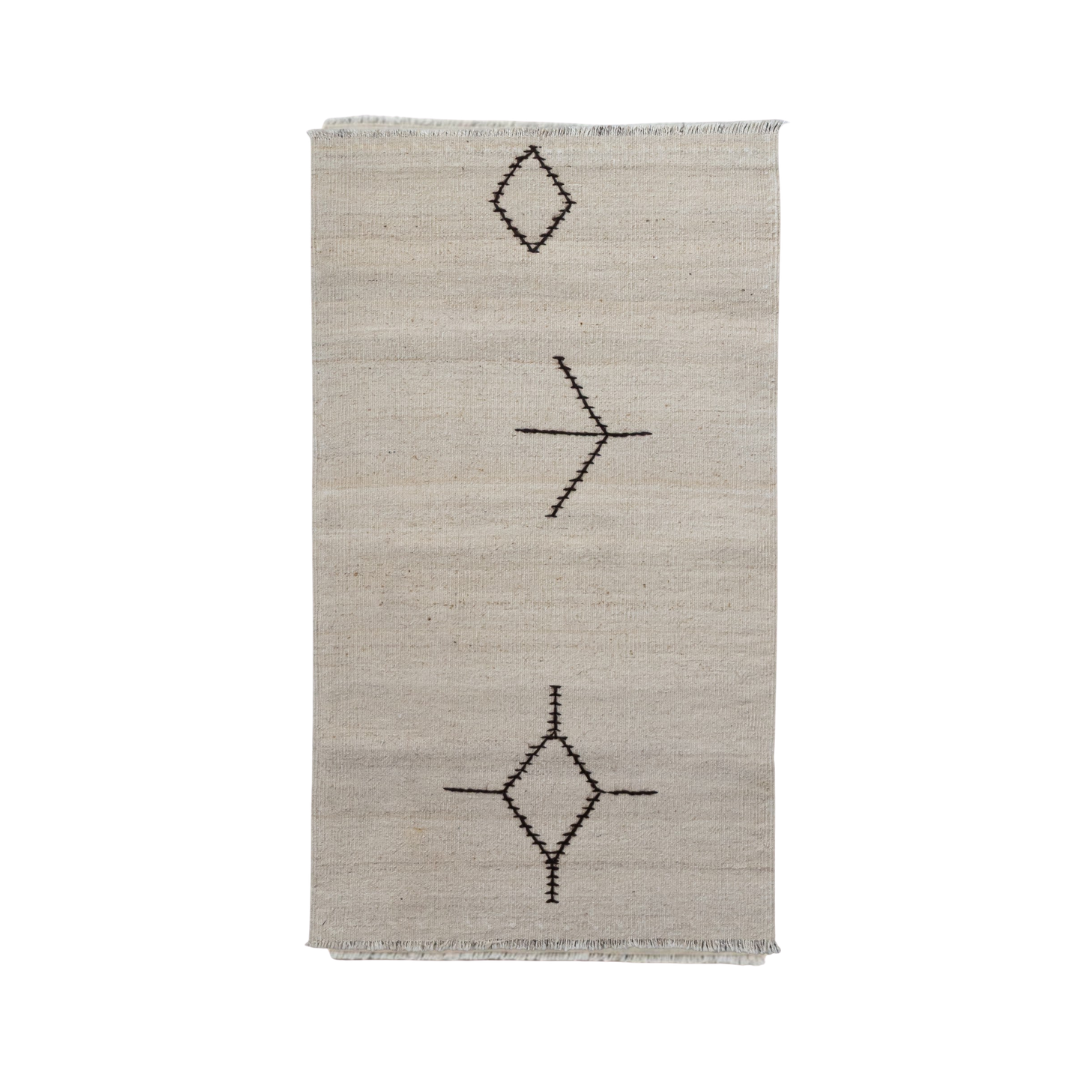 A rectangular natural beige woven rug with a minimalist black geometric pattern of diamonds and lines, featuring short fringe on the top and bottom edges.